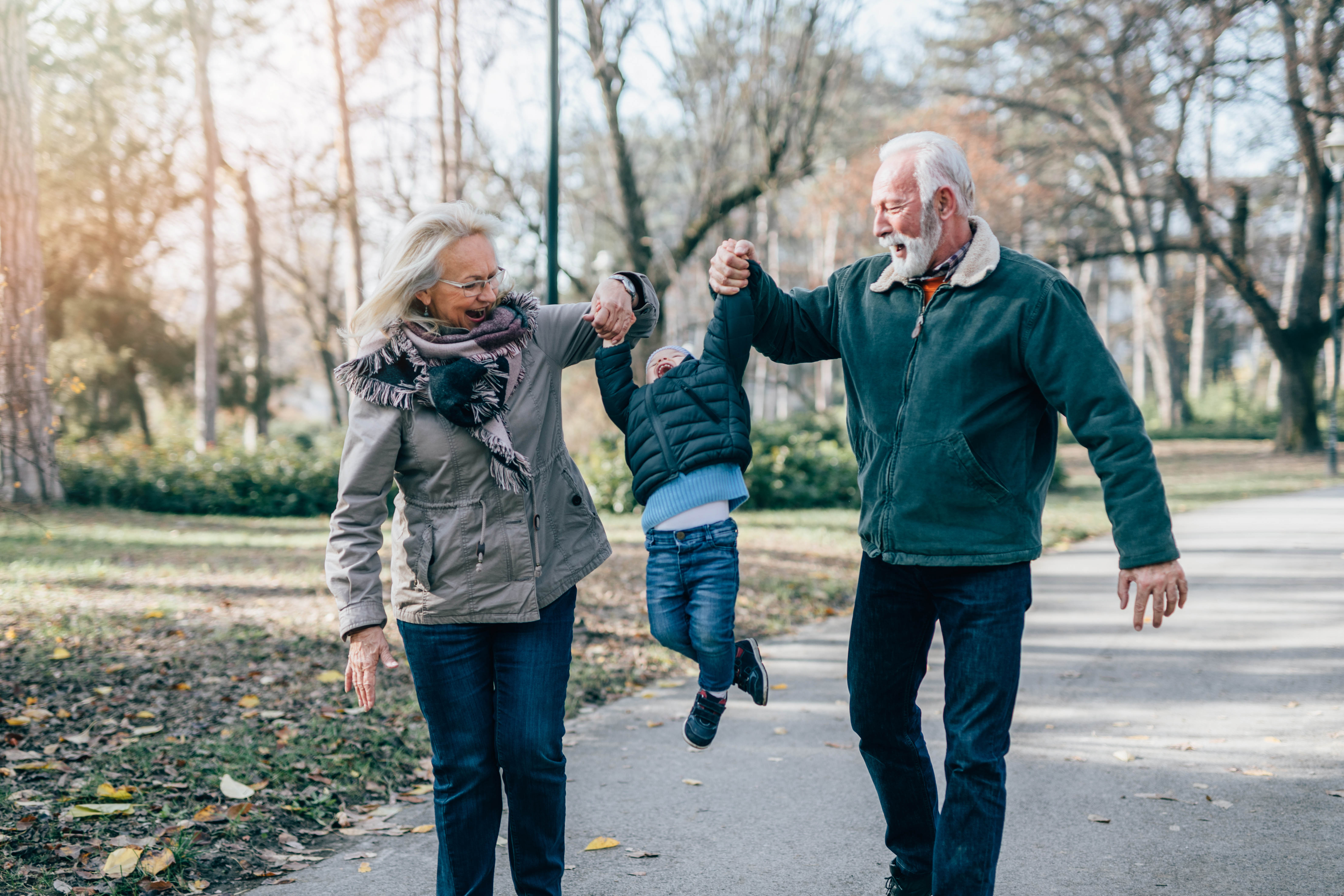 Older grandparents walking outside with their grandchild between them, swinging them by their hands